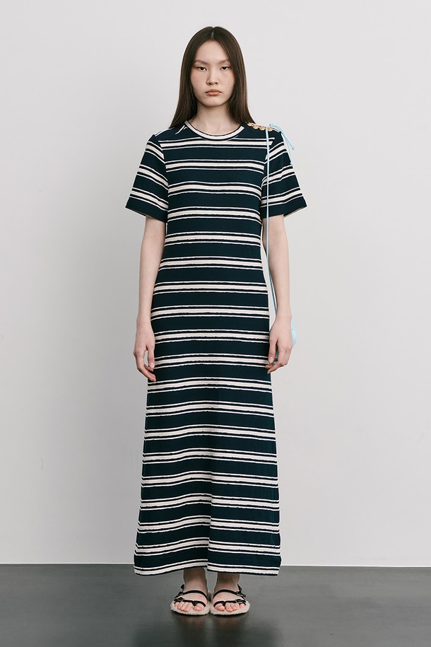네이비 컬러의 스트라이프 자카드 니트 원피스입니다. 부드러운 Cotton 100% 소재로 제작되었으며, 봄, 여름 시즌에 어울리는 얇은 두께감과 A라인 핏, 라운드넥 디자인이 특징입니다. 허리를 잘록하게 잡아주는 실루엣과 밑단으로 갈수록 퍼지는 스커트 라인, 옆 네크 라인의 로고 금속 단추 디테일로 미니멀하면서도 클래식한 무드를 연출합니다.
