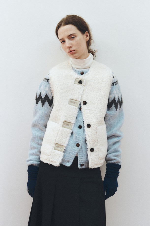 아이보리 컬러의 리버시블 셔링 베스트입니다. 양털과 쉬어링 소재로 제작되어 부드러운 촉감과 두꺼운 두께감으로 따뜻하게 착용할 수 있습니다. 가을, 겨울 시즌에 어울리는 레귤러 핏의 민소매 베스트로, 버튼 여밈 방식과 무지 디자인이 클래식하고 미니멀한 스타일을 연출합니다. 양면 착용이 가능하여 다양한 스타일로 활용할 수 있는 실용적인 아우터입니다. 데일리룩을 완성하는 데 적합한 아이템입니다.
