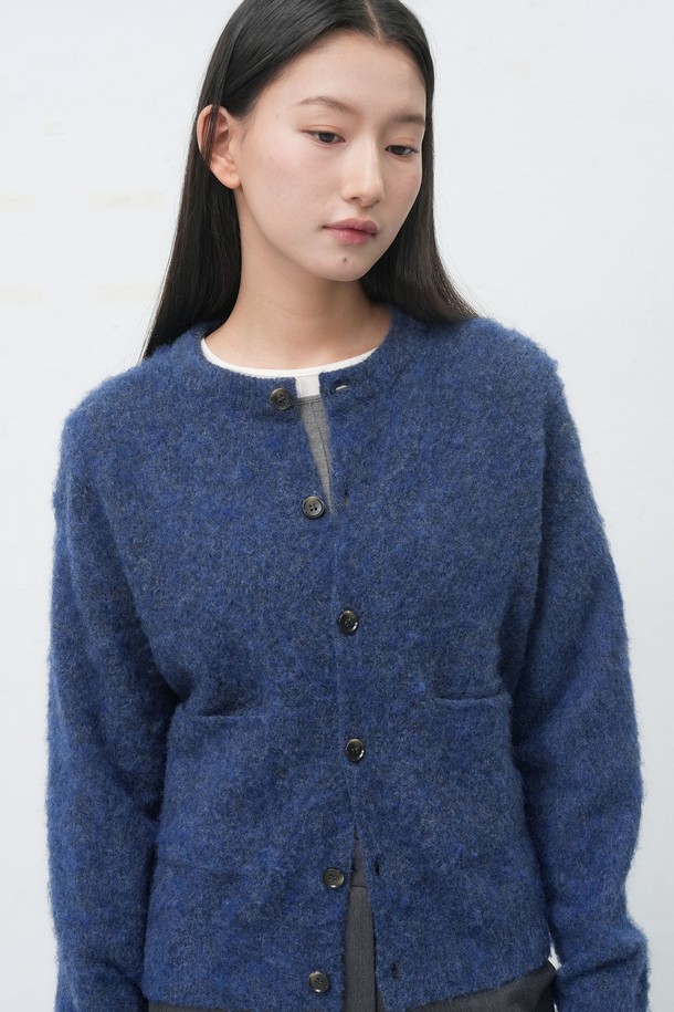 **[25FW] UNISEX 헤어리 니트 포켓 가디건**은 부드러운 울 소재로 제작되어 따뜻하고 포근한 착용감을 선사합니다. 가을과 겨울에 어울리는 두꺼운 두께감과 긴 소매 기장으로 보온성을 높였으며, 넉넉한 레귤러 핏으로 편안하게 착용할 수 있습니다. 캐주얼, 클래식, 미니멀 스타일을 모두 소화 가능하며, 무지 디자인과 네이비 컬러로 다양한 룩에 활용하기 좋습니다. 싱글 버튼 여밈과 포켓, 헤어리 텍스처 디테일이 돋보이며, 출근룩과 모임룩 등 TPO에 구애받지 않고 즐겨 입을 수 있습니다.
