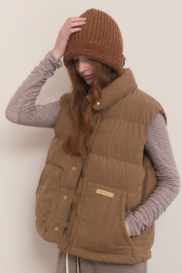 따뜻함과 스타일을 모두 갖춘 코듀로이 오버핏 패딩 베스트입니다. 부드러운 코듀로이 소재에 넉넉한 오버핏으로 편안한 착용감을 선사하며, 겨울철에도 따뜻하게 입을 수 있도록 패딩 안감을 더했습니다. 하이넥 디자인과 지퍼 여밈으로 보온성을 높였으며, 크롭 기장으로 다리가 길어 보이는 효과를 줍니다. 캐주얼, 미니멀, 클래식 등 어떤 스타일에도 잘 어울리는 브라운 컬러의 베이직한 디자인으로, 가을, 겨울 시즌 데일리룩에 활용하기 좋습니다.
