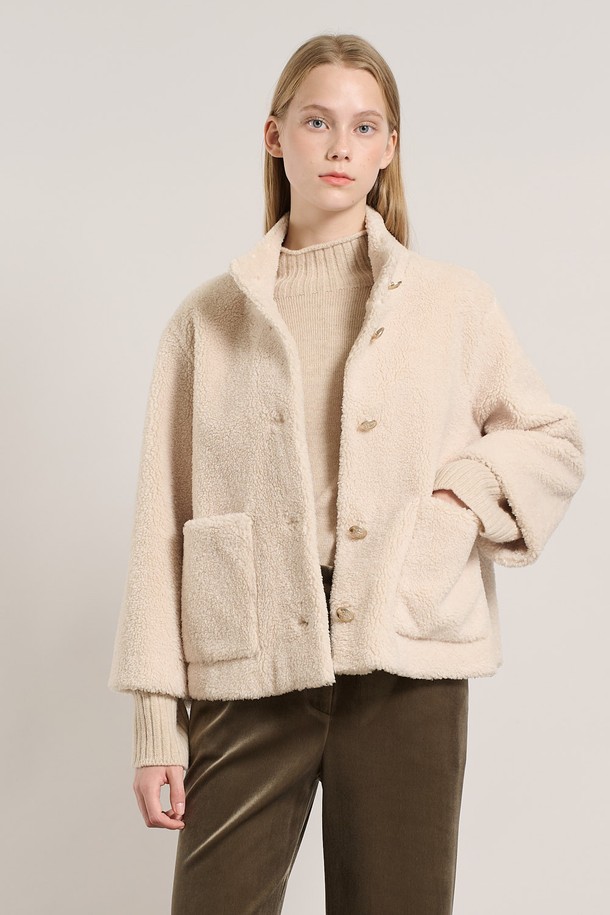 [25WT] 밴드넥 FAKE 무스탕 - IVORY A5WAF81513은 부드러운 촉감의 인조 가죽 소재로 제작된 여성용 무스탕입니다. 밴드넥 디자인과 크롭 기장으로 캐주얼하고 베이직한 스타일을 연출하며, 겨울철 따뜻하게 착용할 수 있습니다. 아이보리 컬러의 무지 디자인에 레귤러 핏으로 어떤 옷에도 쉽게 매치할 수 있습니다. 안감은 퍼 소재로 되어 있어 보온성을 높였으며, 긴 소매와 버튼 여밈 방식이 특징입니다.