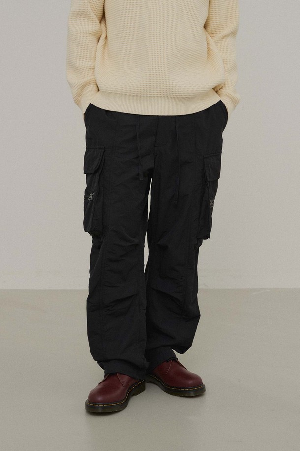 블랙 컬러의 파라슈트 팬츠입니다. 나일론 소재로 제작되어 봄, 가을에 착용하기 좋으며, 뻣뻣한 촉감과 와이드, 루즈핏으로 편안한 착용감을 선사합니다. 허리 밴딩과 밑단 스트링, 카고 포켓 디테일이 돋보이며, 캐주얼, 스트릿, 미니멀 스타일을 모두 소화할 수 있습니다. 여행룩, 캠핑룩 등 다양한 TPO에 활용 가능하며, 무지 디자인으로 어떤 상의와도 매치하기 용이합니다.
