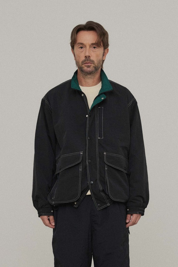 콘트라스트 헌팅 재킷_블랙은 남성용 아우터로, 봄과 가을에 착용하기 좋은 레귤러핏 재킷입니다. 블랙 컬러의 무지 패턴으로 캐주얼, 클래식, 미니멀 스타일을 연출하기 좋으며, 데이트룩과 가을 나들이룩에 적합합니다. 폴리에스테르 소재의 보통 두께감으로 제작되었으며, 하이넥 디자인과 2WAY 지퍼, 배색 안감, 이중 아웃포켓 등의 디테일이 특징입니다. 손목 스냅 조절 및 밑단 스트링으로 핏 조절이 가능하며, 긴 소매 기장과 후면 하단 포인트 라벨로 디자인의 완성도를 높였습니다.
