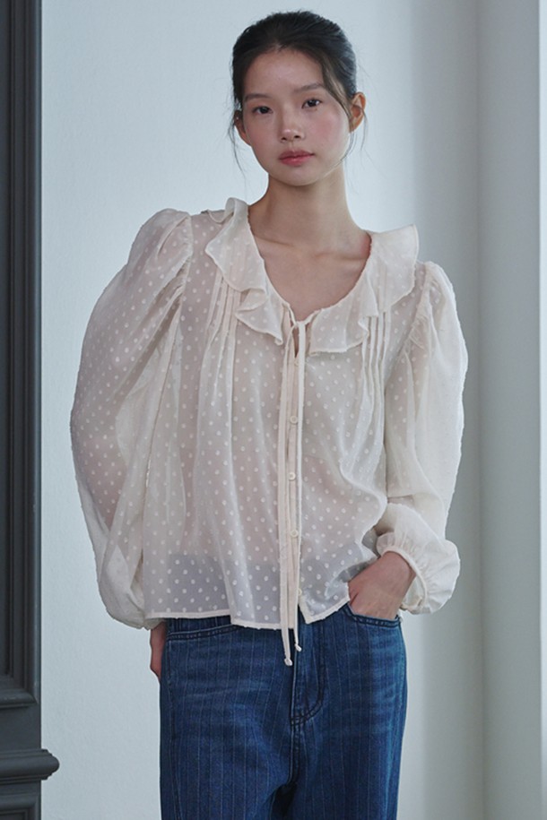 **러플 시스루 도트 블라우스_아이보리**는 페미닌하고 우아한 무드를 연출하는 여성 블라우스입니다. 부드러운 폴리에스테르 소재로 제작되어 봄, 여름, 가을 계절에 착용하기 좋으며, 얇은 두께감으로 시원하게 입을 수 있습니다. 라운드 넥과 긴 소매, 레귤러 핏으로 디자인되었으며, 러플 넥 라인과 스트링 디테일이 여성스러운 포인트를 더합니다. 중앙 버튼 여밈과 시스루 소재, 도트 패턴이 특징이며, 데이트룩, 카페룩, 모임룩 등 다양한 TPO에 클래식, 로맨틱, 미니멀 스타일로 연출하기 좋습니다.
