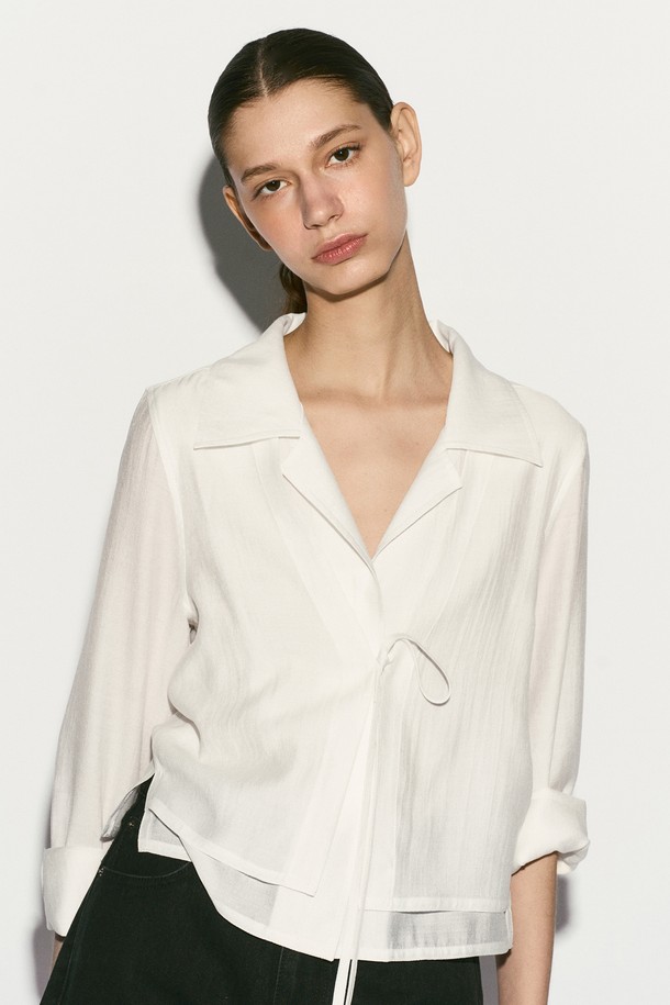 TIE FRONT 레이어드 셔츠는 여성스러운 무드를 연출하는 셔츠/블라우스입니다. 부드러운 촉감의 레이온, 실크, 폴리에스테르 혼방 소재로 제작되어 봄, 여름 시즌에 시원하게 착용하기 좋습니다. 은은한 광택감이 돋보이는 화이트 컬러에 이중 레이어드 디자인과 리본 디테일, 자개 로고 버튼 장식이 더해져 모던하면서도 엘레강스한 스타일을 완성합니다. 레귤러핏과 숄카라, 긴 소매, 크롭 기장으로 디자인되었으며, 데이트룩, 카페룩, 모임룩 등 다양한 TPO에 클래식, 미니멀, 로맨틱 스타일로 코디하기 좋습니다.
