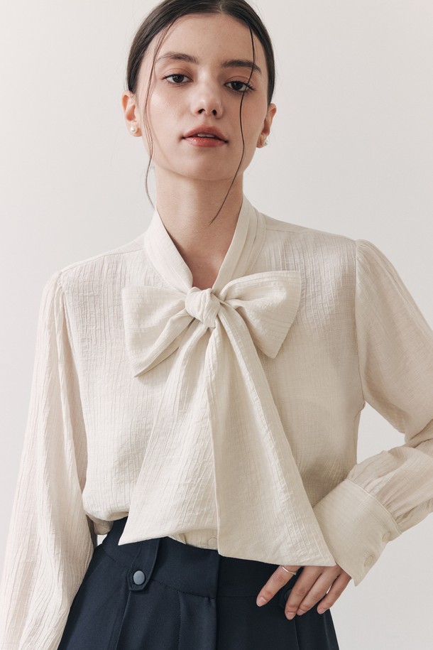 **웨이브 리본 블라우스 / 아이보리**

우아하고 엘레강스한 무드의 여성 블라우스입니다. 아이보리 컬러에 웨이브 텍스처 소재가 돋보이며, 3단 플리츠 타이 디자인과 리본 디테일이 사랑스러운 포인트를 더합니다. 루즈핏으로 편안하면서도 볼륨감 있는 실루엣을 연출하며, 봄, 여름 시즌 데이트룩, 모임룩, 카페룩 등 다양한 TPO에 활용하기 좋습니다. 부드러운 촉감의 레이온과 나일론 혼방 소재로 제작되었으며, 약간의 비침이 있습니다. 클래식, 로맨틱, 미니멀 스타일을 즐겨 입는 분들께 추천합니다.
