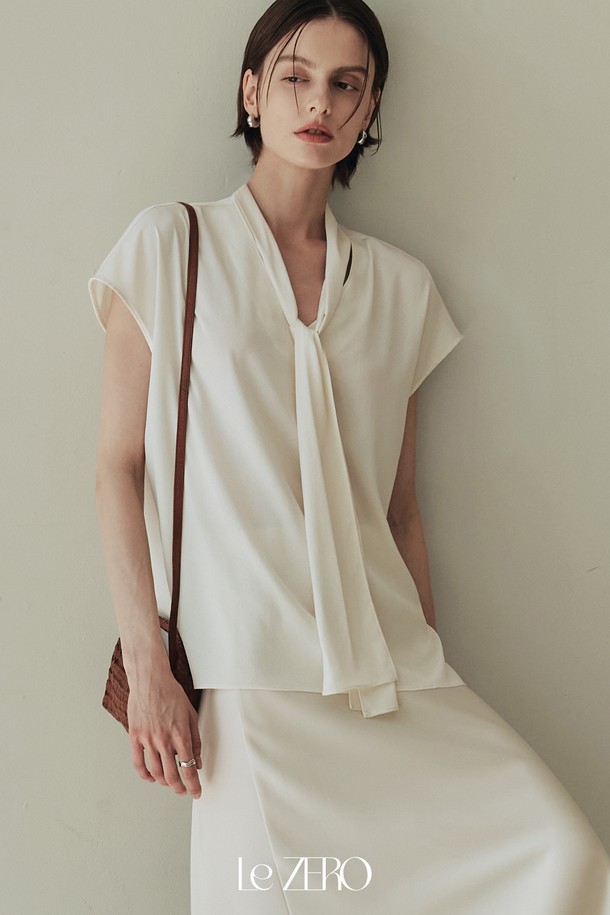 르제로 글로우 타이 블라우스는 아이보리 컬러의 여성 블라우스로, 봄, 여름 시즌에 어울리는 데일리 아이템입니다. 실키한 소재감과 은은한 광택이 특징이며, 넥 라인 셔링 디테일과 넓은 숄더 라인, 돌먼 소매 디자인으로 우아하고 미니멀한 스타일을 연출합니다. 약간의 비침과 신축성이 있으며, 루즈핏으로 편안하게 착용할 수 있는 타이넥 블라우스입니다.
