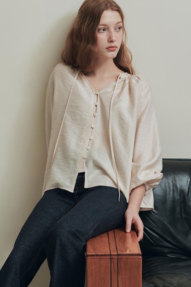 엘리스 블라우스 / 베이지는 여성스러운 무드를 연출하는 블라우스입니다. 부드러운 레이온과 나일론 혼방 소재로 제작되어 봄, 여름 시즌에 시원하게 착용할 수 있습니다. 은은한 광택과 세로 스트라이프 패턴이 우아한 분위기를 더하며, 브이넥 디자인과 루즈핏 실루엣으로 편안함을 선사합니다. 앞중심 버튼, 리본 스트랩, 소매단 셔링과 밴딩 디테일이 돋보이며, 오피스룩, 데이트룩, 모임룩 등 다양한 TPO에 활용 가능합니다. 클래식, 미니멀, 로맨틱 스타일을 즐겨 입는 분들께 추천합니다.
