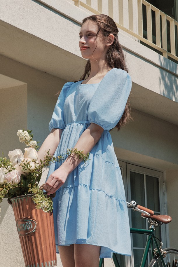 시원한 촉감의 블루 컬러 버블 캉캉 원피스입니다. 체크 패턴의 시어서커 원단과 A라인 핏으로 러블리하고 페미닌한 분위기를 연출하며, 허리끈으로 더욱 여성스러운 실루엣을 완성합니다. 반소매 기장에 스퀘어넥 디자인, 부분 안감 처리로 편안하게 착용 가능하며, 데일리룩과 캐주얼룩에 활용하기 좋습니다.
