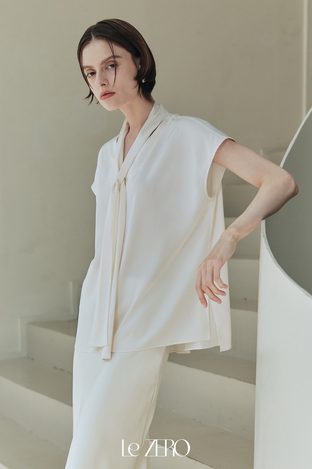 르제로 글로우 타이 블라우스는 아이보리 컬러의 여성 블라우스로, 봄, 여름 시즌에 어울리는 데일리 아이템입니다. 실키한 소재감과 은은한 광택이 특징이며, 넥 라인 셔링 디테일과 넓은 숄더 라인, 돌먼 소매 디자인으로 우아하고 미니멀한 스타일을 연출합니다. 약간의 비침과 신축성이 있으며, 루즈핏으로 편안하게 착용할 수 있는 타이넥 블라우스입니다.
