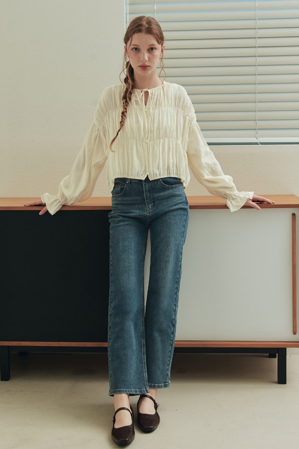 버니 셔링 블라우스 / 크림은 로맨틱한 무드를 연출하는 여성 블라우스입니다. 부드러운 레이온과 나일론 혼방 소재로 제작되어 봄, 여름 시즌에 시원하게 착용하기 좋습니다. 어깨, 가슴, 허리 라인에 셔링 디테일을 더해 여성스러운 실루엣을 강조하며, 리본넥 디자인과 긴 소매 기장으로 우아함을 더했습니다. 크롭 기장과 릴랙스핏으로 편안하면서도 세련된 데일리룩, 데이트룩, 카페룩, 모임룩을 완성해보세요. 반투명 소재와 작은 버튼 디테일, 드롭 숄더 디자인이 은은한 포인트를 더해줍니다.
