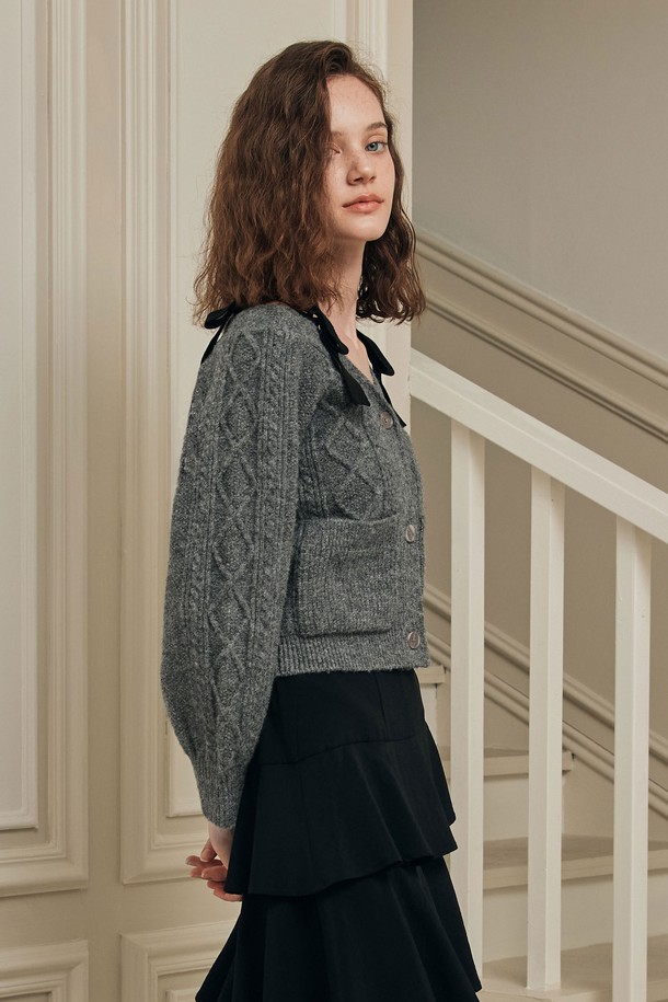 **[2컬러] 프렌치 리본 가디건**은 로맨틱한 무드를 연출하는 여성용 니트 가디건입니다. 부드러운 촉감의 울 블렌드 소재로 제작되었으며, 중간 두께감으로 겨울철 따뜻하게 착용하기 좋습니다. 슬림핏 디자인에 와이드넥으로 여성스러운 실루엣을 강조하며, 트위스트 텍스처 패턴이 특징입니다. 아이보리, 그레이 두 가지 색상으로 출시되었으며, 숄더 리본 스트랩과 볼륨감 있는 소매 라인, 리본 포인트 디테일이 사랑스러운 분위기를 더합니다. 데이트룩, 겨울 데일리룩, 모임룩 등 다양한 TPO에 활용할 수 있습니다.
