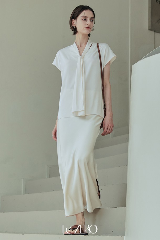 르제로 글로우 타이 블라우스는 아이보리 컬러의 여성 블라우스로, 봄, 여름 시즌에 어울리는 데일리 아이템입니다. 실키한 소재감과 은은한 광택이 특징이며, 넥 라인 셔링 디테일과 넓은 숄더 라인, 돌먼 소매 디자인으로 우아하고 미니멀한 스타일을 연출합니다. 약간의 비침과 신축성이 있으며, 루즈핏으로 편안하게 착용할 수 있는 타이넥 블라우스입니다.
