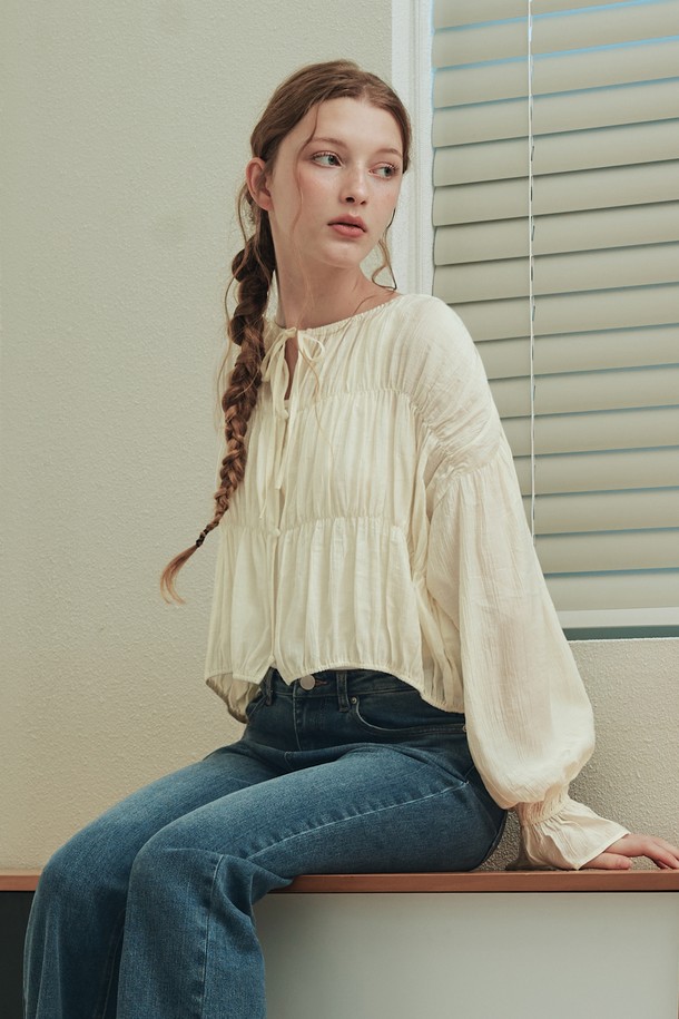 버니 셔링 블라우스 / 크림은 로맨틱한 무드를 연출하는 여성 블라우스입니다. 부드러운 레이온과 나일론 혼방 소재로 제작되어 봄, 여름 시즌에 시원하게 착용하기 좋습니다. 어깨, 가슴, 허리 라인에 셔링 디테일을 더해 여성스러운 실루엣을 강조하며, 리본넥 디자인과 긴 소매 기장으로 우아함을 더했습니다. 크롭 기장과 릴랙스핏으로 편안하면서도 세련된 데일리룩, 데이트룩, 카페룩, 모임룩을 완성해보세요. 반투명 소재와 작은 버튼 디테일, 드롭 숄더 디자인이 은은한 포인트를 더해줍니다.
