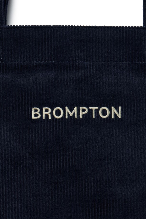 **코듀로이 에코 백 - 네이비 (P255ATO413)**

부드러운 코듀로이 소재와 면, 폴리에스테르 혼방으로 제작된 네이비 컬러의 미디엄 사이즈 에코 백입니다. 심플하고 베이직한 디자인으로 일상, 여행 등 다양한 TPO에 활용하기 좋습니다. 가방 내부에는 텀블러 포켓과 내부 포켓이 있어 실용성을 높였으며, D링을 활용하여 측면 장식을 부착할 수 있습니다. 가볍고 부드러운 촉감으로 편안하게 사용 가능하며, 자수 로고가 디자인 포인트입니다. 스타일은 캐주얼, 미니멀, 클래식 무드를 연출합니다.
