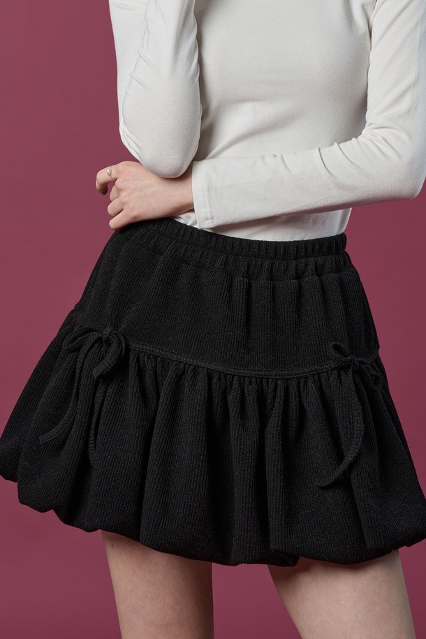 **방한 니트 벌룬 리본 플레어 밴딩 미니스커트 [BLACK] 치마바지 ver.**

따뜻한 겨울과 가을을 위한 여성용 미니스커트입니다. 부드러운 니트 소재로 제작되어 포근한 착용감을 선사하며, 루즈핏 벌룬 디자인과 플레어 스타일로 사랑스러운 분위기를 연출합니다. 허리 밴딩과 리본 디테일이 편안함과 여성스러움을 더하고, 블랙 컬러는 어떤 상의와도 쉽게 매치할 수 있어 활용도가 높습니다. 캐주얼, 미니멀 스타일을 즐겨 입는 분들께 추천하는 아이템입니다.
