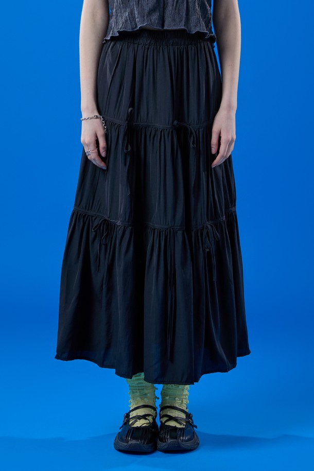 쿨링 기능성 원단으로 제작된 블랙 색상의 롱스커트입니다. 밴딩, 리본, 주름 디테일이 특징이며, 플레어 및 티어드 치마핏으로 페스티벌이나 프레피 스타일을 연출하기에 좋습니다. 여름철 일상에서 시원하고 쾌적하게 착용 가능한 얇은 두께의 롱 플레어스커트입니다.
