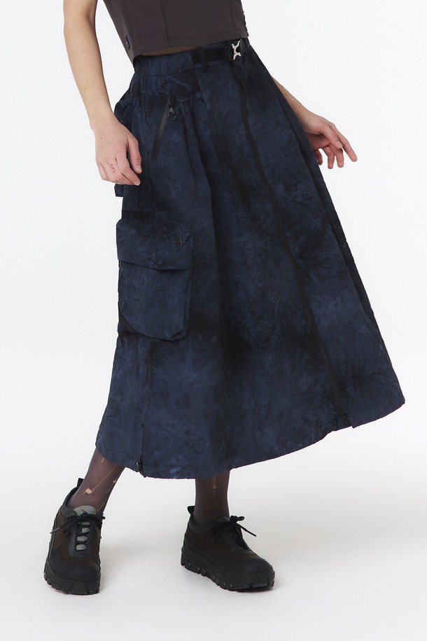 여성용 물나염 셋업 스커트(다크 네이비)_5LB1822는 부드러운 나일론 소재의 A라인 맥시스커트입니다. 스포티하고 캐주얼한 무드를 연출하며, 물나염/타이다이 패턴이 돋보입니다. 방수 기능과 방수 지퍼 포켓, 2-WAY 지퍼, 메탈 버클 디테일이 있으며, 점퍼 5LG1322와 셋업하여 착용 가능합니다.
