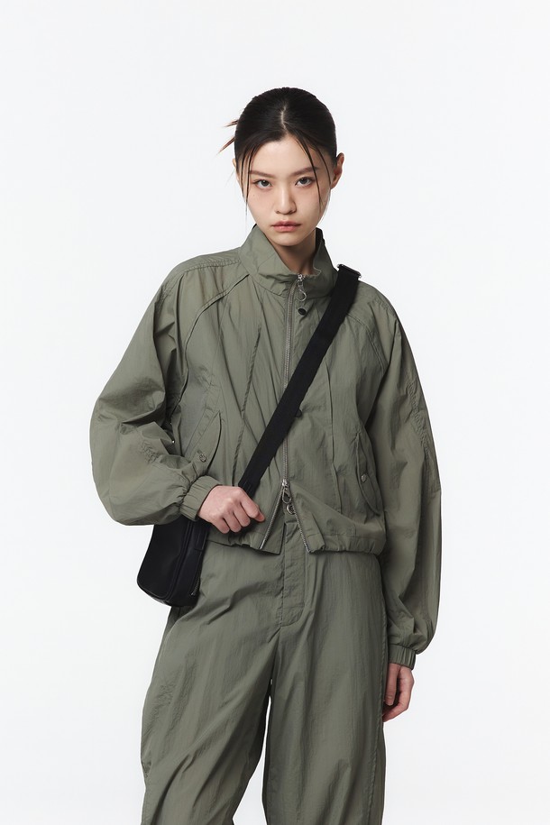 여성용 애쉬 올리브 색상의 긴팔 스탠드 칼라 셋업 점퍼로, 넉넉한 핏과 크롭 기장이 특징입니다. 얇은 나일론 소재로 제작되었으며, 하이넥 스타일과 벌룬 소매, 밑단 스트링으로 캐주얼한 무드를 연출할 수 있습니다. 지퍼와 스냅 여밈 방식이며, 바람막이 형태로 봄철 일상복으로 활용하기 좋습니다.
