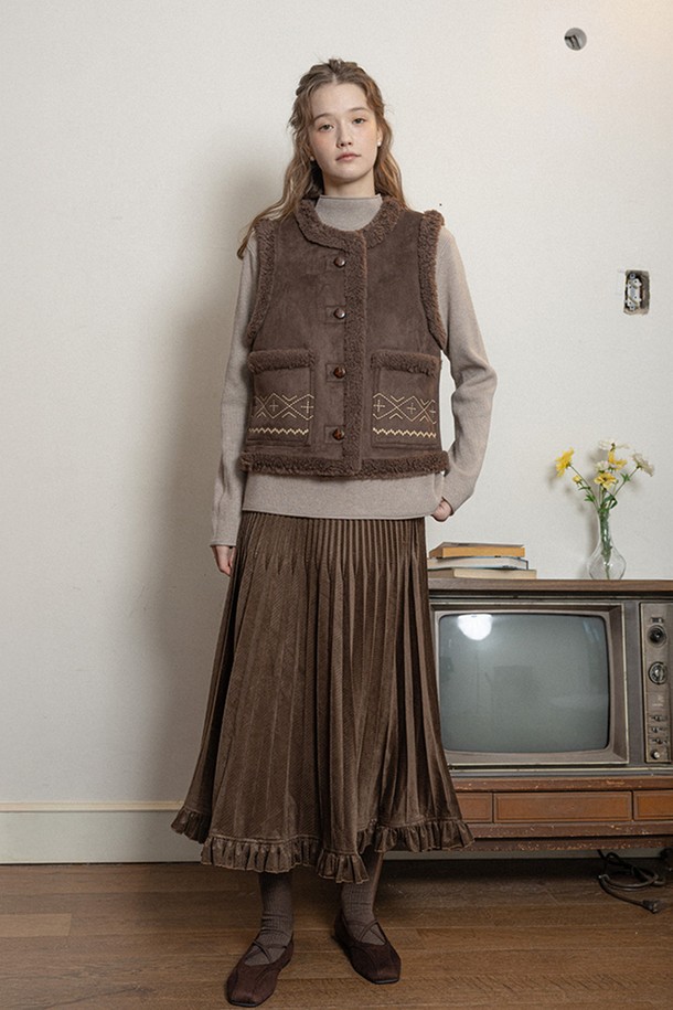 다크 브라운 컬러의 여성용 '윈터 클래식 머스탱 베스트'입니다. 부드러운 무스탕 소재로 제작되어 겨울철 따뜻함을 선사하며, 크롭 기장과 레귤러 핏으로 세련된 실루엣을 연출합니다. 클래식과 캐주얼 스타일을 모두 소화할 수 있으며, 자수 무늬와 퍼 디테일이 포인트로 더해져 고급스러운 분위기를 더합니다. 버튼 여밈 방식으로 편안하게 착용 가능하며, 민소매 디자인으로 다양한 레이어드 룩을 연출하기 좋습니다.
