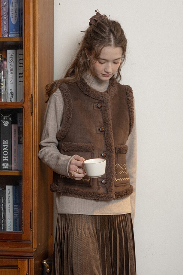 다크 브라운 컬러의 여성용 '윈터 클래식 머스탱 베스트'입니다. 부드러운 무스탕 소재로 제작되어 겨울철 따뜻함을 선사하며, 크롭 기장과 레귤러 핏으로 세련된 실루엣을 연출합니다. 클래식과 캐주얼 스타일을 모두 소화할 수 있으며, 자수 무늬와 퍼 디테일이 포인트로 더해져 고급스러운 분위기를 더합니다. 버튼 여밈 방식으로 편안하게 착용 가능하며, 민소매 디자인으로 다양한 레이어드 룩을 연출하기 좋습니다.
