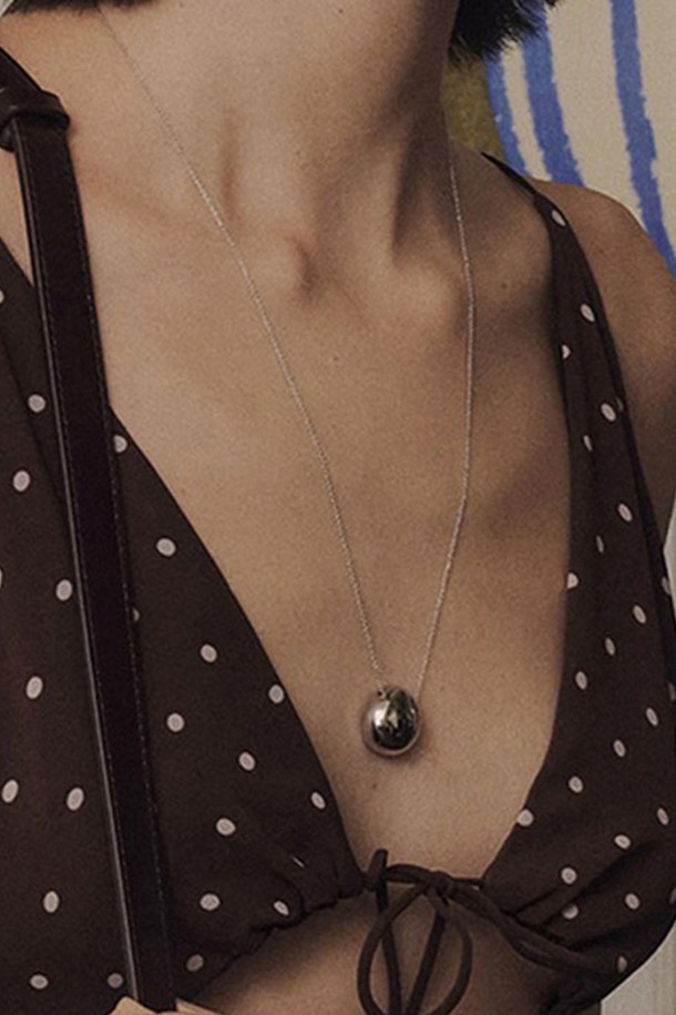 페블 펜던트 목걸이 [실버]는 미니멀하고 모던한 스타일을 추구하는 여성들을 위한 목걸이입니다. 볼륨감 있는 비정형 라운드 형태의 펜던트 디자인이 특징이며, 고광택 실버 컬러로 세련된 느낌을 더했습니다. 얇은 체인과 가벼운 무게감으로 편안한 착용감을 제공하며, 일상 및 데이트룩, 모임룩 등 다양한 TPO에 활용하기 좋습니다. 브라스 소재로 제작되어 은은한 광택을 자랑하며 시크하고 클래식한 무드를 연출합니다.
