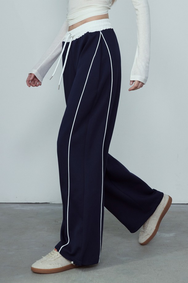 CONTOUR LINE 투웨이 밴딩 와이드 팬츠_NFTR5307는 편안함과 스타일을 동시에 잡은 공용 와이드핏 트레이닝 팬츠입니다. 부드러운 촉감의 폴리에스테르와 면 혼방 소재로 제작되어 사계절 내내 활용 가능하며, 밴딩 허리 디자인으로 편안한 착용감을 제공합니다. 세로 파이핑 라인과 허리 배색 디테일이 스포티한 무드를 더하고, 하단 스토퍼 장식으로 활동성을 높였습니다. 일상, 스포츠 활동은 물론, 동네 마실룩, 피트니스룩, 여행룩 등 다양한 TPO에 맞춰 캐주얼하고 미니멀한 스타일을 연출할 수 있습니다. 
