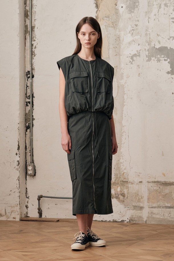 여성용 D GREY 컬러 필드 카고 스커트 SET입니다. 나일론 소재의 H라인 카고스커트와 민소매 베스트가 세트로 구성되어 있으며, 캐주얼하고 스포티한 무드를 연출합니다. 2-WAY 지퍼 디테일, 아웃포켓 디자인, 밑단 개더링 디테일이 돋보이며, 사계절 아웃도어 및 일상에서 활용하기 좋습니다.
