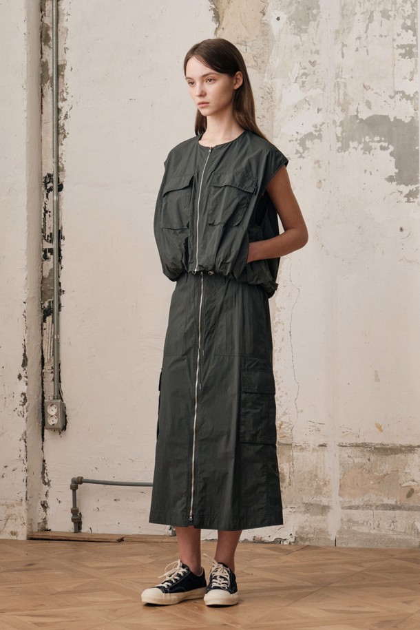 여성용 D GREY 컬러 필드 카고 스커트 SET입니다. 나일론 소재의 H라인 카고스커트와 민소매 베스트가 세트로 구성되어 있으며, 캐주얼하고 스포티한 무드를 연출합니다. 2-WAY 지퍼 디테일, 아웃포켓 디자인, 밑단 개더링 디테일이 돋보이며, 사계절 아웃도어 및 일상에서 활용하기 좋습니다.
