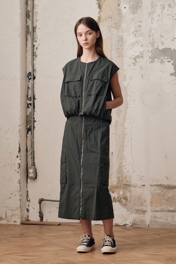 여성용 D GREY 컬러 필드 카고 스커트 SET입니다. 나일론 소재의 H라인 카고스커트와 민소매 베스트가 세트로 구성되어 있으며, 캐주얼하고 스포티한 무드를 연출합니다. 2-WAY 지퍼 디테일, 아웃포켓 디자인, 밑단 개더링 디테일이 돋보이며, 사계절 아웃도어 및 일상에서 활용하기 좋습니다.
