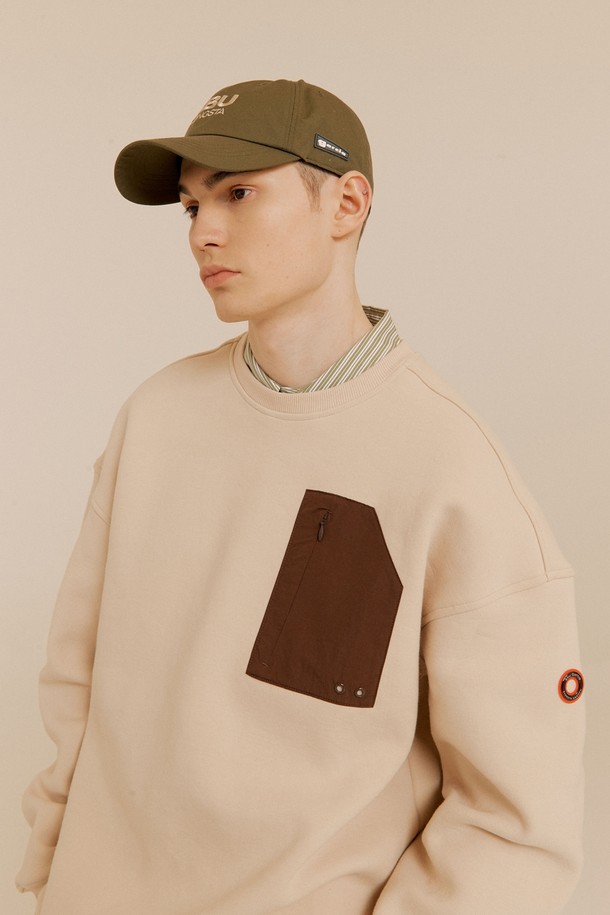 라이트 베이지 컬러의 부클 자수 맨투맨입니다. 면혼방 소재로 제작되어 부드러운 촉감을 선사하며, 캐주얼한 스타일을 연출하기 좋습니다. 뒷면에는 로고 부클 자수, 팔꿈치 패치 디자인, 소매단/밑단 립 처리, 소매 서클 와펜 등의 디테일이 돋보입니다. 라운드넥 디자인에 가슴 우측 지퍼 포켓이 있어 실용적이며, 봄, 여름 시즌 동네 마실룩, 여행룩, 소풍룩에 활용하기 좋습니다. 
