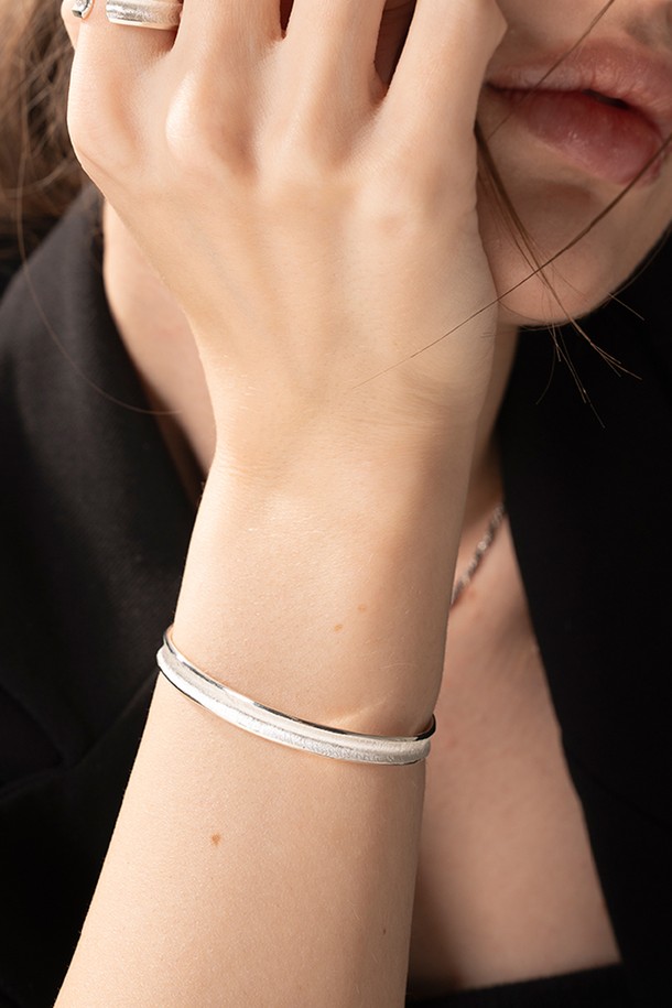 세련된 무드의 린넨스톤 뱅글팔찌입니다. 부드러운 곡선 텍스처와 무광 실버 925 소재가 돋보이며, 한쪽 끝에는 큐빅 지르코니아 장식이 세팅되어 은은한 포인트를 더합니다. 약 5.8mm x 2.5mm의 콤팩트한 사이즈로, 데일리 룩 또는 모임룩에 미니멀, 클래식, 시크한 스타일을 연출하기 좋습니다. 양면 착용이 가능하여 다양한 분위기를 연출할 수 있습니다.

