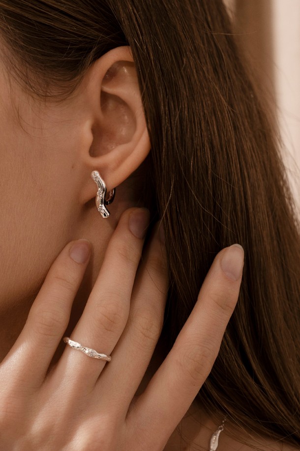 **웨이브 블룸 이어링**은 자연스러운 곡선 디자인이 돋보이는 여성용 이어링입니다. 실버925 소재에 큐빅 지르코니아를 세팅하여 은은한 광택을 더했으며, 매트한 실버 표면 질감이 고급스러운 분위기를 자아냅니다. 미니멀하면서도 우아한 스타일로, 데이트룩이나 카페룩에 세련된 포인트를 줄 수 있습니다. 심플한 디자인과 불규칙한 표면 질감이 조화롭게 어우러져 일상 속 특별함을 선사합니다.
