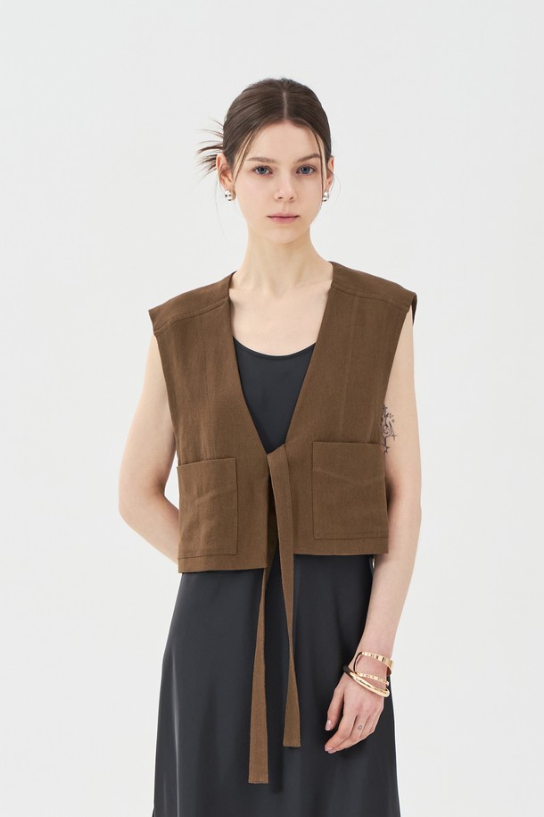 브라운 색상의 린넨 브이넥 베스트는 여름철 일상에서 클래식하고 캐주얼한 스타일을 연출하기에 좋습니다. 린넨, 레이온, 면 혼방 소재로 제작되었으며, 브이넥 디자인과 아웃포켓, 스티치 디테일, 허리 스트랩이 특징입니다. 레귤러핏과 루즈핏의 중간 형태로 민소매 디자인이며, 크롭 기장으로 제작되었습니다.

