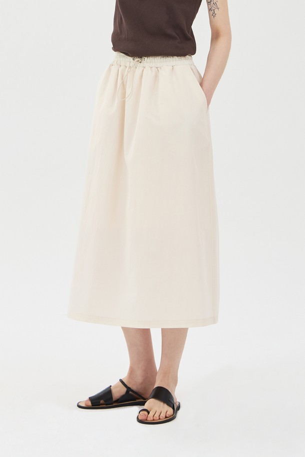 아이보리 컬러의 드로우스트링 밴딩 롱 스커트입니다. 면과 나일론 혼방 소재로 제작되어 얇고 바스락거리는 촉감이 특징이며, 여름철에도 시원하게 착용할 수 있습니다. 허리 밴딩과 드로우스트링으로 편안한 착용감을 선사하며, A라인 핏과 사이드 포켓, 안감 처리가 되어 있어 실용성을 더했습니다. 
