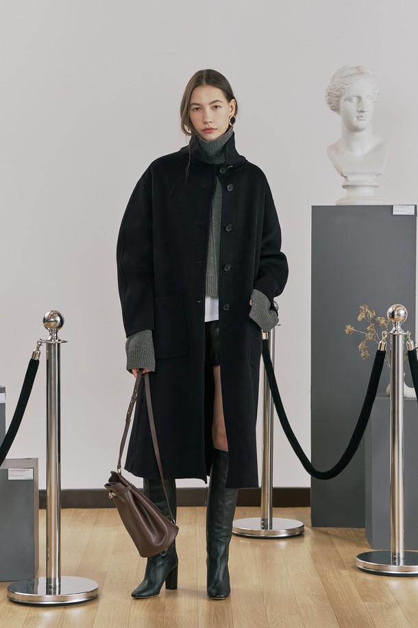 **울 핸드메이드 하이넥 롱 코트 블랙**

우아함과 미니멀함을 동시에 선사하는 여성용 울 핸드메이드 하이넥 롱 코트입니다. 부드러운 촉감의 울 소재로 제작되어 겨울철에도 따뜻하게 착용할 수 있으며, 롱 기장과 루즈핏으로 편안한 착용감을 제공합니다. 하이넥 디자인과 싱글 버튼 여밈 방식이 클래식하면서도 시크한 분위기를 연출합니다. 안감 처리가 되어 있어 고급스러운 마감과 착용감을 더했고, 아웃포켓과 소뿔 단추 디테일로 실용성을 높였습니다. 오피스룩, 출근룩, 모임룩 등 다양한 TPO에 활용 가능하며, 어떤 스타일에도 세련되게 매치할 수 있는 필수 아이템입니다.
