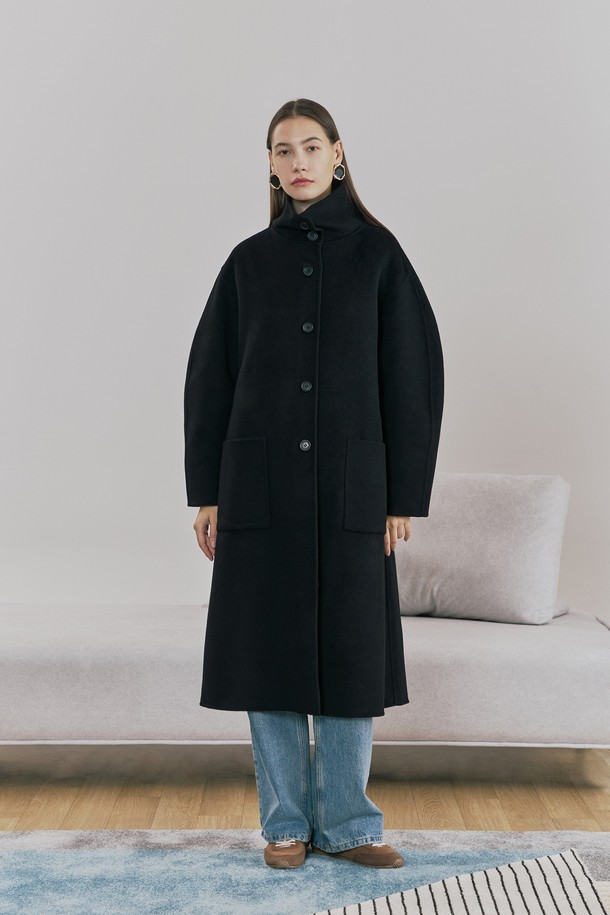 **울 핸드메이드 하이넥 롱 코트 블랙**

우아함과 미니멀함을 동시에 선사하는 여성용 울 핸드메이드 하이넥 롱 코트입니다. 부드러운 촉감의 울 소재로 제작되어 겨울철에도 따뜻하게 착용할 수 있으며, 롱 기장과 루즈핏으로 편안한 착용감을 제공합니다. 하이넥 디자인과 싱글 버튼 여밈 방식이 클래식하면서도 시크한 분위기를 연출합니다. 안감 처리가 되어 있어 고급스러운 마감과 착용감을 더했고, 아웃포켓과 소뿔 단추 디테일로 실용성을 높였습니다. 오피스룩, 출근룩, 모임룩 등 다양한 TPO에 활용 가능하며, 어떤 스타일에도 세련되게 매치할 수 있는 필수 아이템입니다.
