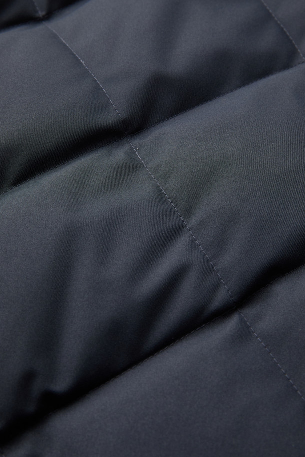 듀크 구스다운 파카는 겨울철 캐주얼 및 일상룩에 적합한 남성용 아우터입니다. 네이비 색상의 무지 디자인으로, 후드 탈착이 가능하며 경량 구스다운 충전재를 사용하여 보온성을 높였습니다. 지퍼와 버튼으로 여밀 수 있으며, 중기장 기장의 레귤러핏으로 제작되어 편안한 착용감을 제공합니다. 출근룩과 여행룩 모두 소화 가능한 미니멀하고 베이직한 스타일의 파카입니다. 
