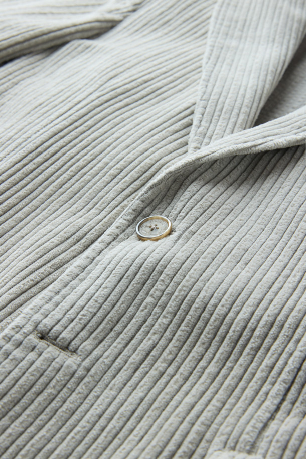 **SANTANIELLO(산타니엘로) 볼드 코듀로이 재킷**은 남성용 자켓으로, 캐주얼, 클래식, 미니멀 스타일을 모두 아우르는 매력적인 아이템입니다. 봄, 가을에 착용하기 적합하며, 출근룩으로도 활용할 수 있습니다. 그레이 컬러의 레귤러핏 자켓으로, 볼드한 코듀로이 원단과 싱글 버튼 디테일이 특징입니다. 두께감 있는 코듀로이 소재는 뻣뻣한 촉감을 선사하며, 긴 소매 기장으로 제작되었습니다. 
