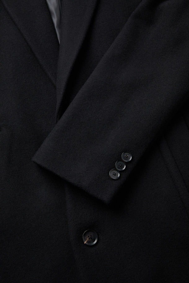 블랙 캐시미어 블렌디드 싱글 코트는 남성 고객을 위한 가을/겨울용 아우터입니다. 울, 캐시미어, 폴리에스테르, 나일론, 레이온, 코튼 등 다양한 소재를 혼방하여 부드러운 촉감과 두꺼운 두께를 자랑합니다. 클래식하고 미니멀한 스타일로, 오피스룩, 비즈니스 캐주얼, 모임룩 등 TPO에 맞춰 시크하게 연출할 수 있습니다. 너치드 라펠, 2버튼, 사이드 다트, 숄더 다트, 어깨 패드, 포켓 스티치 디테일이 돋보이는 레귤러핏 싱글 코트입니다. 긴 소매 기장의 무지 디자인으로 어떤 스타일에도 쉽게 매치할 수 있습니다.
