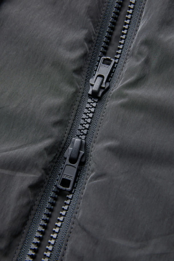 다크그레이 컬러의 탈부착 패딩 재킷입니다. 나일론과 폴리에스테르 혼방 소재로 제작되어 겨울철에도 따뜻하게 착용 가능하며, 오버핏으로 편안한 착용감을 선사합니다. 탈부착 가능한 소매 디자인으로 다양한 스타일 연출이 용이하며, 하이넥 디자인과 YKK 2-Way 지퍼, 스트링, 스토퍼 디테일이 특징입니다. 캐주얼, 미니멀, 시티보이 룩에 잘 어울리며, 출근룩과 여행룩 모두 소화 가능한 실용적인 아이템입니다.

