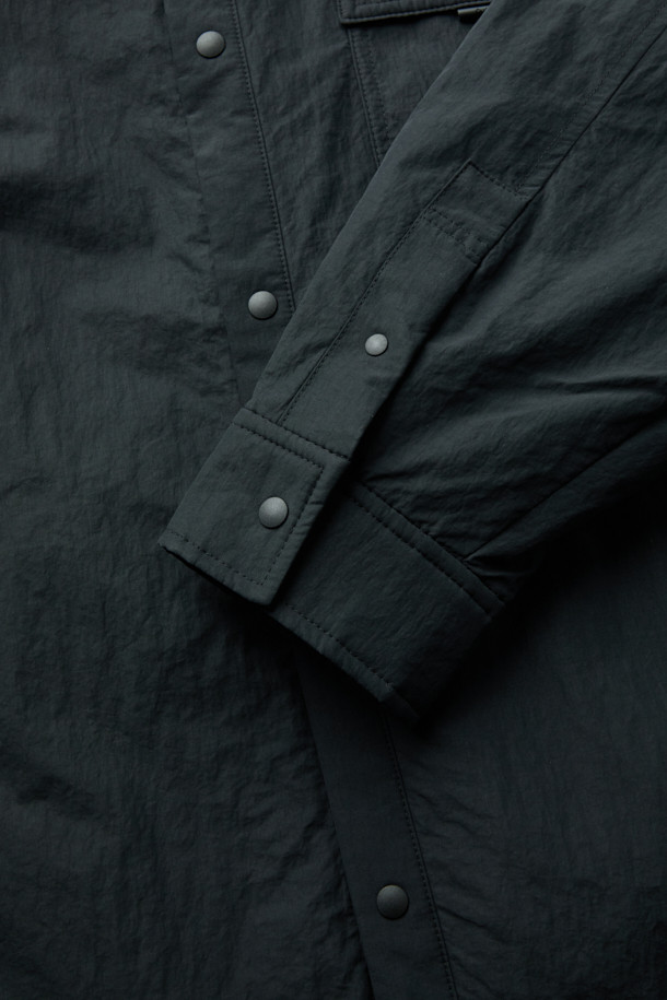 블랙 패딩 아우터 셔츠는 남성용 캐주얼 패딩셔츠입니다. 가을과 겨울에 착용하기 좋으며, 차이나칼라와 긴 소매, 무지 패턴으로 미니멀한 스타일을 연출합니다. 초경량 하스 충전재를 사용하여 보온성을 높였으며, 퀼팅 안감으로 부드러운 착용감을 제공합니다. 밑단 스트링 디테일과 우레탄 라벨 포인트가 특징이며, 핏은 오버핏으로 제작되었습니다. 면과 나일론 혼방 소재로 제작되어 편안함과 내구성을 동시에 갖췄습니다.
