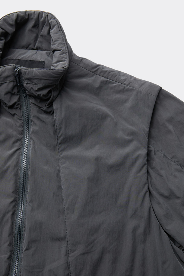 다크그레이 컬러의 탈부착 패딩 재킷입니다. 나일론과 폴리에스테르 혼방 소재로 제작되어 겨울철에도 따뜻하게 착용 가능하며, 오버핏으로 편안한 착용감을 선사합니다. 탈부착 가능한 소매 디자인으로 다양한 스타일 연출이 용이하며, 하이넥 디자인과 YKK 2-Way 지퍼, 스트링, 스토퍼 디테일이 특징입니다. 캐주얼, 미니멀, 시티보이 룩에 잘 어울리며, 출근룩과 여행룩 모두 소화 가능한 실용적인 아이템입니다.
