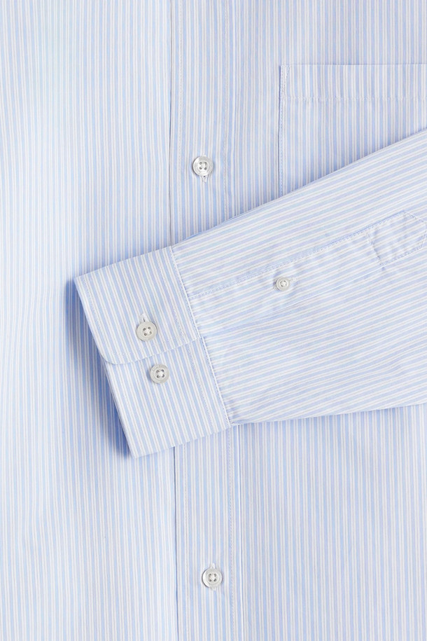 "줄무늬 셔츠 (줄무늬 셔츠)"는 산뜻한 라이트 블루 컬러의 스트라이프 셔츠입니다. 면 소재의 릴랙스 핏으로 제작되어 편안한 착용감을 선사하며, 봄, 여름 시즌에 적합합니다. 차이나칼라와 긴 소매, 가슴 패치 포켓, '재미있는' 자수 디테일이 특징이며, 버튼 여밈 소매와 앞면 6개의 로고 각인 버튼으로 디자인의 완성도를 높였습니다. 비즈니스 캐주얼 및 출근룩, 캐주얼, 클래식, 미니멀 스타일 모두 소화 가능한 활용도 높은 아이템입니다.
