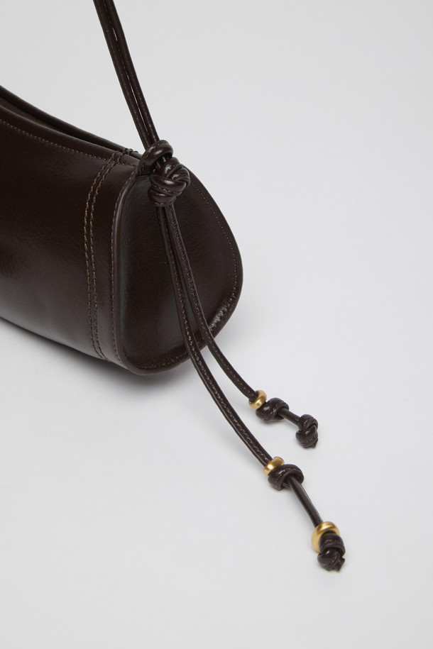 에스프레소 컬러의 Knotted case bag(노티드 케이스 백)은 부드러운 가죽 소재의 여성용 크로스백입니다. 미디엄 사이즈의 반원 형태에 매듭 디테일과 버클 장식이 포인트이며, 세련된 세미 크레센트 쉐입이 돋보입니다. 지퍼형 잠금 방식으로 소지품을 안전하게 보관할 수 있으며, 숄더 스트랩이 포함되어 있어 편리하게 착용 가능합니다. 클래식, 미니멀, 시크 스타일을 즐기는 분들에게 데이트룩, 모임룩, 출근룩 등 다양한 TPO에 맞춰 활용하기 좋은 아이템입니다.
