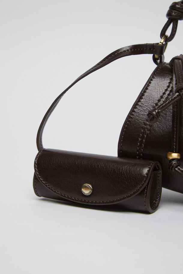 에스프레소 컬러의 Knotted case bag(노티드 케이스 백)은 부드러운 가죽 소재의 여성용 크로스백입니다. 미디엄 사이즈의 반원 형태에 매듭 디테일과 버클 장식이 포인트이며, 세련된 세미 크레센트 쉐입이 돋보입니다. 지퍼형 잠금 방식으로 소지품을 안전하게 보관할 수 있으며, 숄더 스트랩이 포함되어 있어 편리하게 착용 가능합니다. 클래식, 미니멀, 시크 스타일을 즐기는 분들에게 데이트룩, 모임룩, 출근룩 등 다양한 TPO에 맞춰 활용하기 좋은 아이템입니다.
