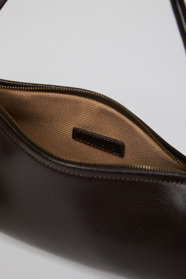 에스프레소 컬러의 Knotted case bag(노티드 케이스 백)은 부드러운 가죽 소재의 여성용 크로스백입니다. 미디엄 사이즈의 반원 형태에 매듭 디테일과 버클 장식이 포인트이며, 세련된 세미 크레센트 쉐입이 돋보입니다. 지퍼형 잠금 방식으로 소지품을 안전하게 보관할 수 있으며, 숄더 스트랩이 포함되어 있어 편리하게 착용 가능합니다. 클래식, 미니멀, 시크 스타일을 즐기는 분들에게 데이트룩, 모임룩, 출근룩 등 다양한 TPO에 맞춰 활용하기 좋은 아이템입니다.
