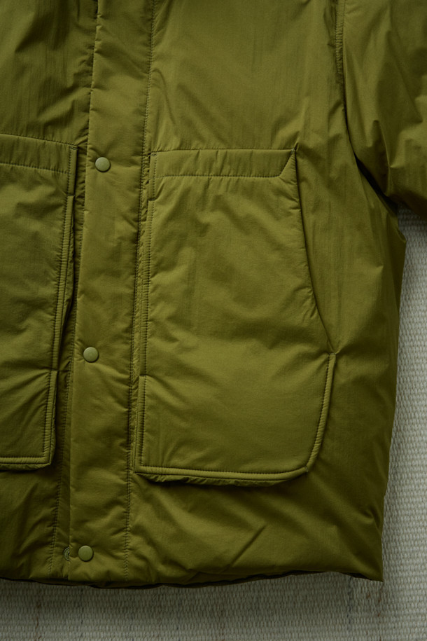 FFC x DOCUMENT (FFC x 도큐먼트) 피셔맨 셔팅 구스 다운 재킷은 겨울철 데일리룩에 적합한 미니멀하면서도 캐주얼한 스타일의 아우터입니다. 올리브 및 카키 색상으로 출시되었으며, 가볍고 따뜻한 구스다운 90/10 충전재를 사용하여 보온성과 경량성을 동시에 잡았습니다. 셔츠형 디자인에 투웨이 지퍼 여밈 방식과 입체 포켓 디테일을 더해 실용성을 높였으며, 여유 있는 어깨 라인과 루즈핏으로 편안한 착용감을 선사합니다. 부드러운 촉감의 나일론 소재로 제작되었으며, 긴 소매 기장과 두꺼운 두께감으로 추운 겨울에도 따뜻하게 입을 수 있습니다.
