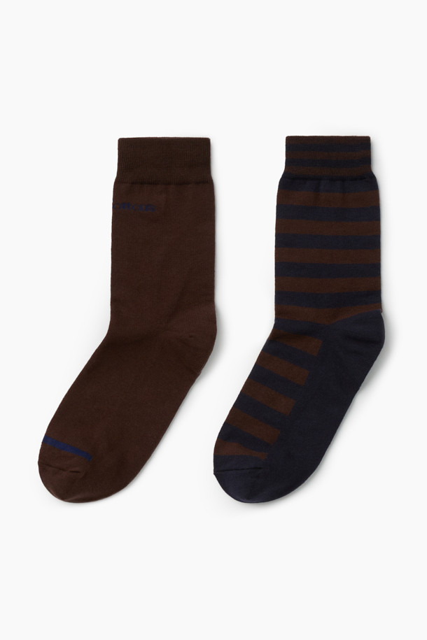 **2족 세트_캐주얼 블럭 양말**

가을, 겨울에 착용하기 좋은 2족 세트 캐주얼 블럭 양말입니다. 면과 스판덱스 혼방 소재로 제작되어 편안한 착용감과 신축성을 제공하며, 발목 부분에는 스판사를 적용하여 흘러내림을 방지합니다. 브라운과 네이비 컬러, 로고 및 스트라이프 패턴의 조화로 클래식하면서도 캐주얼한 스타일을 연출할 수 있습니다. 논슬립 기능과 톤온톤 배색, 실리콘 프린트 디자인으로 포인트를 더했습니다. 겨울 데일리룩, 산책룩, 집콕룩 등 다양한 TPO에 활용해보세요.
