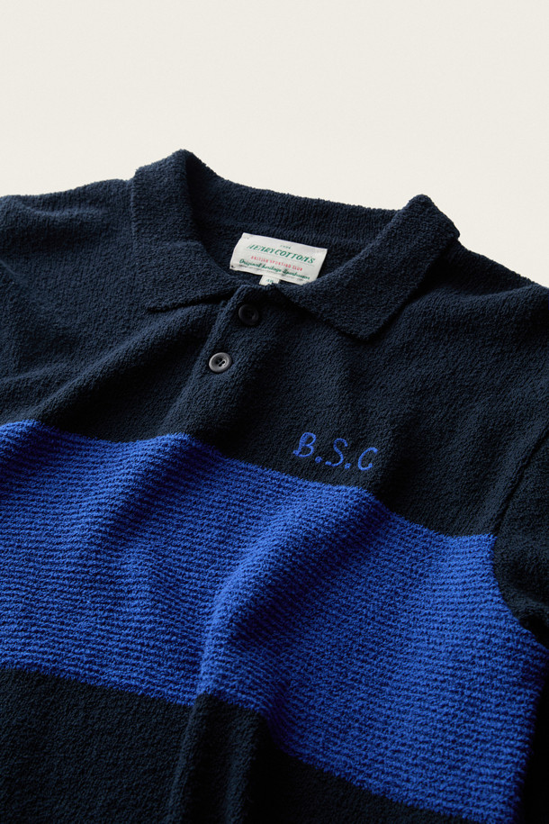 **British Sporting Club 컬러 블록 폴로 니트**

네이비와 블루 컬러 배색이 돋보이는 [British Sporting Club] (브리티시 스포팅 클럽)의 컬러 블록 폴로 니트입니다. 부드러운 촉감의 부클사 니트 소재로 제작되어 가을 시즌에 따뜻하게 착용하기 좋습니다. 루즈핏으로 편안하며, 긴 소매와 폴로넥 디자인이 클래식하면서도 스포티한 무드를 연출합니다. 가슴 부분에는 B.S.C 자수 로고가, 소매와 밑단은 립 조직 마감으로, 단추 여밈 디테일이 돋보입니다. 데이트룩, 카페룩, 가을 나들이룩 등 다양한 스타일링에 활용해 보세요.
